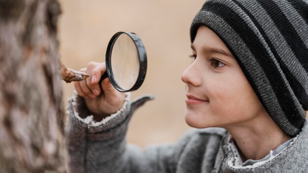 Side view little boy looking through a magnifier