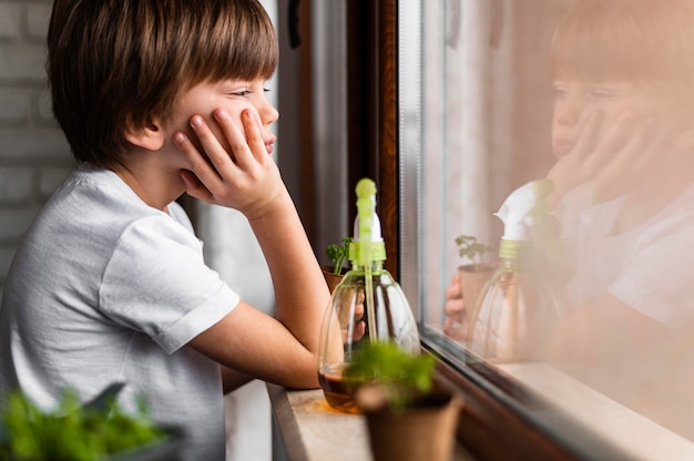 Side view of little boy looking through the window with water spray for crops