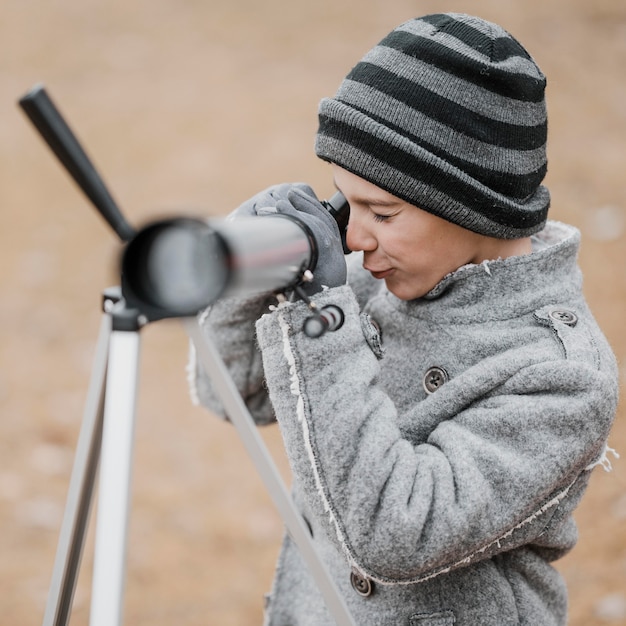 Side view little boy using a telescope