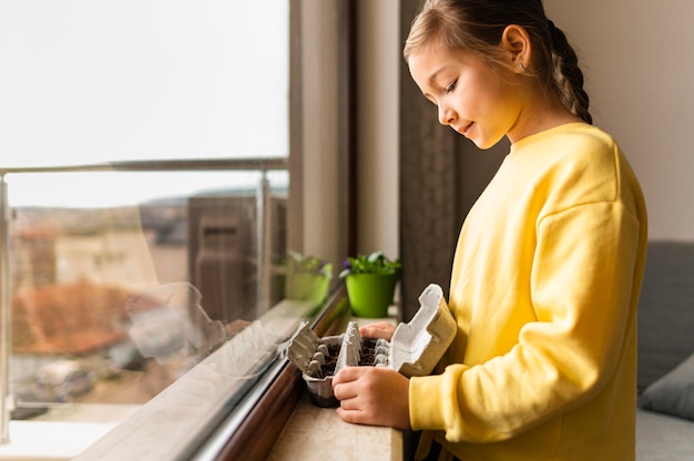 Free photo side view of little girl holding planted seeds in egg carton