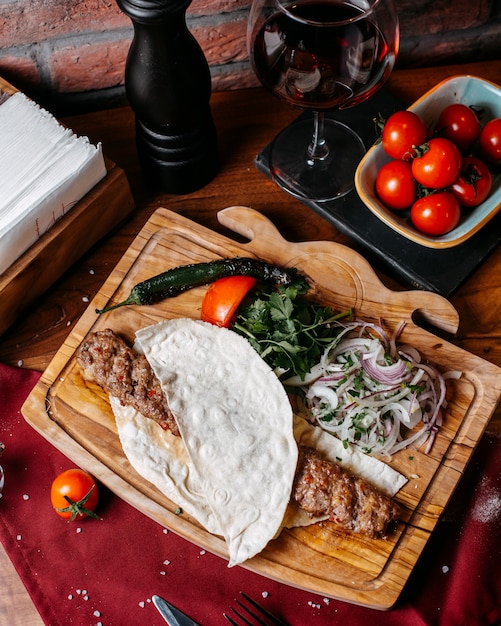 Free photo side view of lula kebab with onions herbs and vegetables on a wooden board