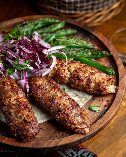 Free photo side view of lula kebab with red onions  sumakh and grilled green chili peppers on a wooden board