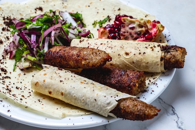 Side view lulya kebab with pomegranate greens red onion and dried barberry on pita