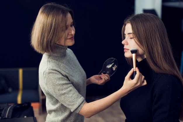 Free photo side view makeup artist applying powder on model