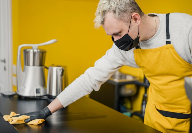 Free photo side view of male barista with medical mask cleaning table surface