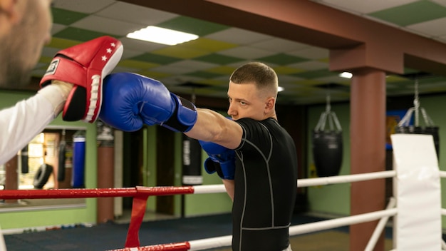 Side view of male boxer with gloves exercising with trainer