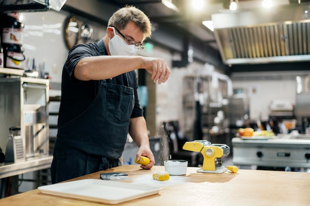 Free photo side view of male chef with mask seasoning pasta