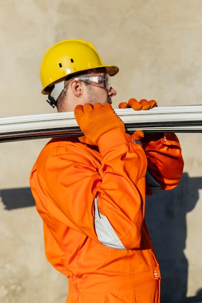 Free photo side view of male laborer with hard hat carrying steel