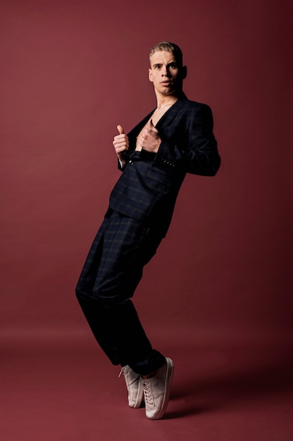 Free photo side view of male performer in suit and sneakers posing while holding blazer open