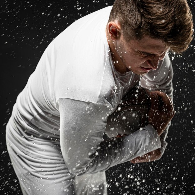 Side view of male rugby player with ball and water splashes