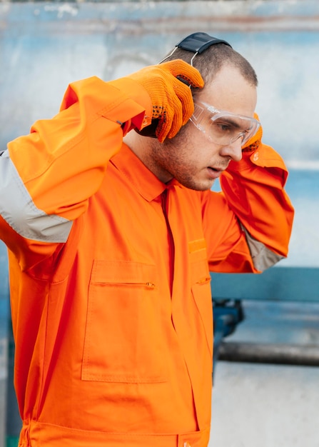 Free photo side view of male worker in uniform with protective glasses and headphones