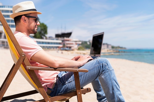 Side view of man in beach chair working on laptop