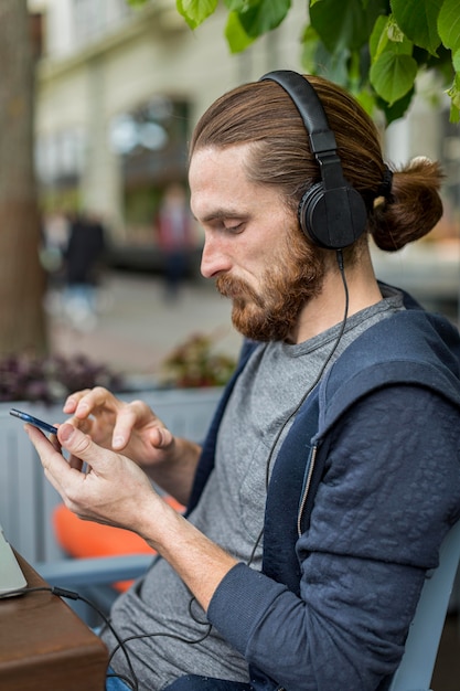 Free photo side view of man at a city terrace with smartphone and headphones