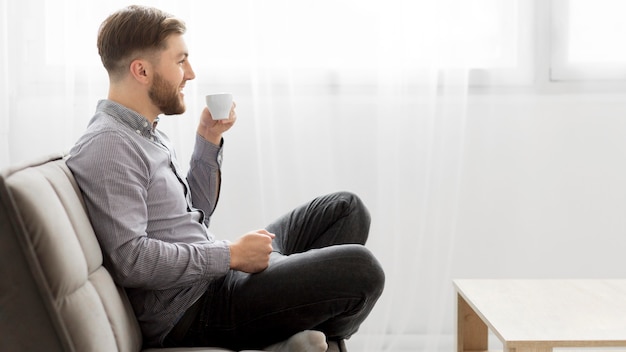 Side view man on couch drinking coffee