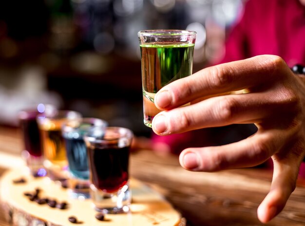 Side view a man drinks colorful shots with coffee beans on a piece of wood