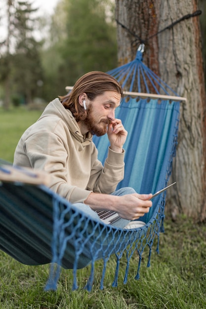 Free photo side view of man in hammock with laptop