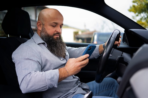 Free photo side view man holding smartphone in car