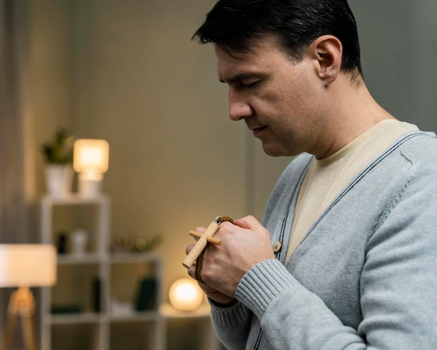 Side view of man holding wooden cross and praying