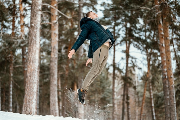 Side view of man jumping outdoors in nature during winter