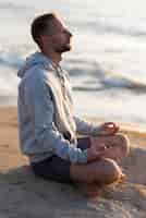 Free photo side view man meditating on the beach