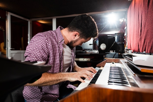 Side view man playing the keyboard in the studio