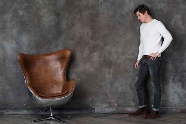 Free photo side view man posing next to leather chair