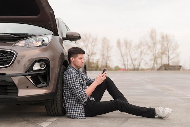 Side view man sitting next to broken car