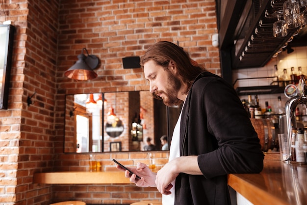 Side view of man standing on bar with phone