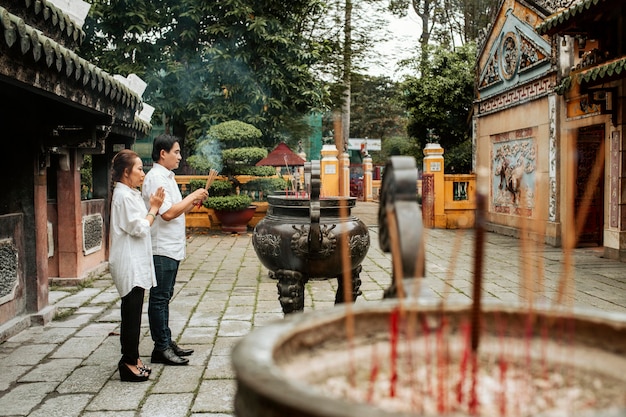 Side view of man and woman praying at the temple with burning incense