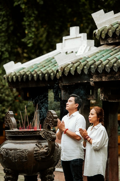 Side view of man and woman praying at the temple with burning incense