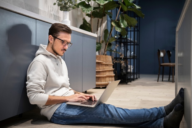 Free photo side view of man working from home while sitting on the floor with laptop