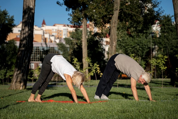 Free photo side view of mature couple practicing yoga outdoors