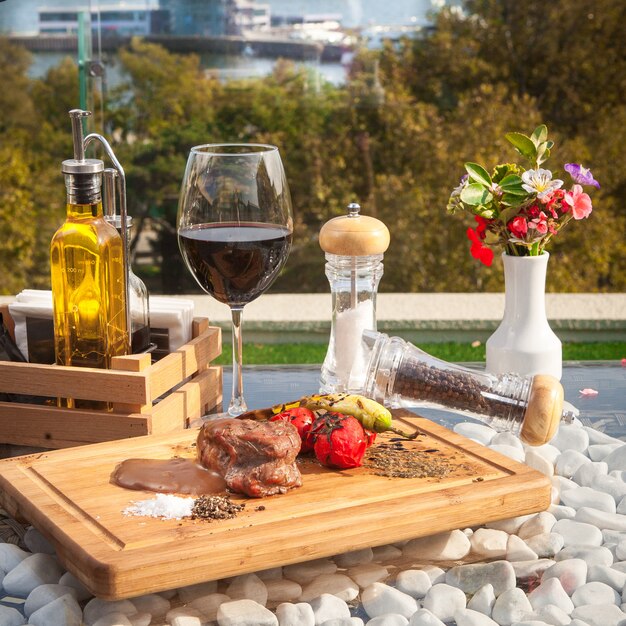 Side view meat steak with pomato on wooden board with glass of wine on glass table with sea view