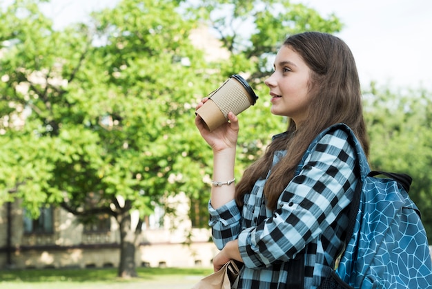 Side view medium shot teenage girl drinking from papercup