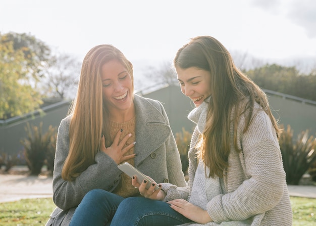 Free Photo side view medium shot of two young women looking at the phone in the park