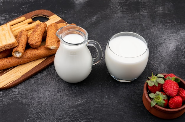 Free photo side view of milk with crackers and strawberry on black surface horizontal