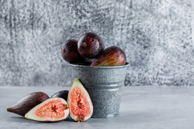 Free photo side view mission figs and halves in bucket on textured background. horizontal space for text