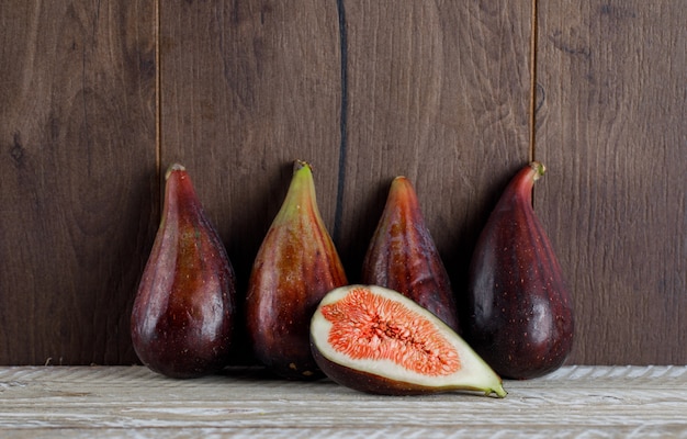 Free photo side view mission figs with fig half on wooden table. horizontal