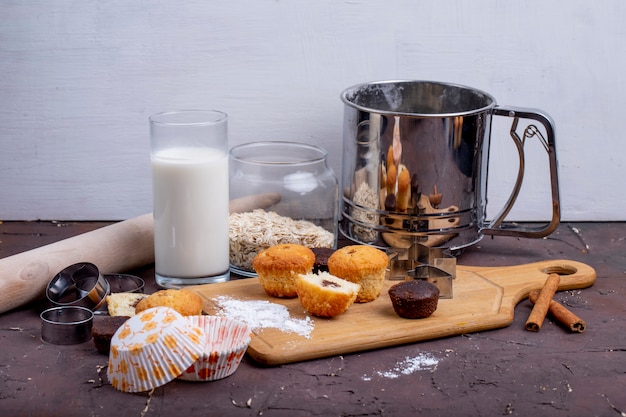 Side view of muffins and a glass of milk on a wooden cutting board