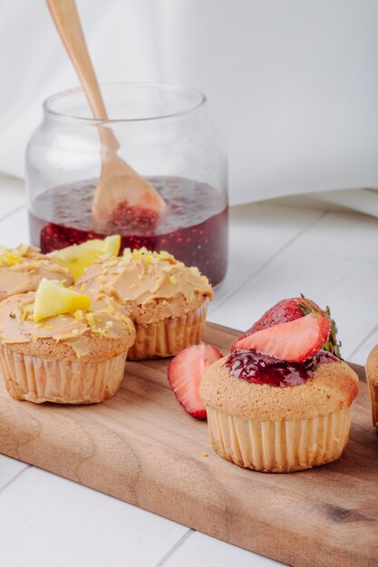 Side view muffins with strawberries and lemon on a board with a jar of jam