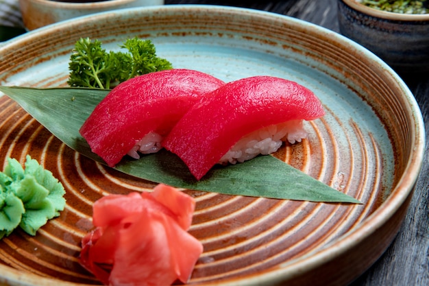 Side view of nigiri sushi with tuna on bamboo leaf served with pickled ginger slices and wasabi on a plate