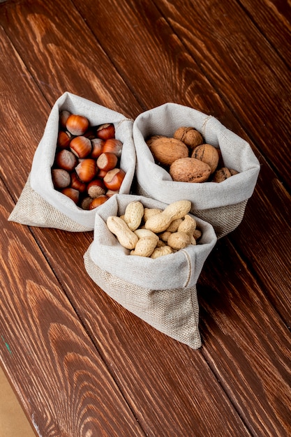 Side view of nuts in sacks walnuts peanuts and hazelnuts in shell on wooden background