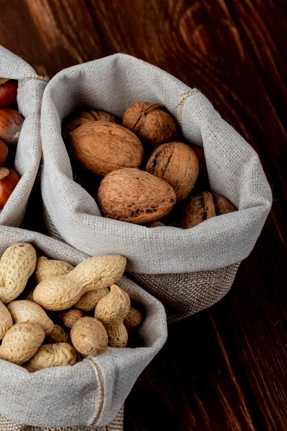 Side view of nuts in sacks walnuts peanuts and hazelnuts in shell on wooden background