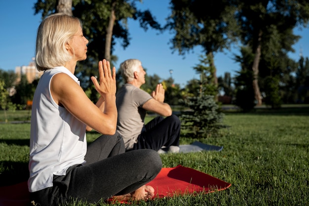 Side view of older couple practicing yoga outdoors with copy space