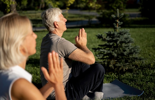 Free photo side view of older couple practicing yoga outside