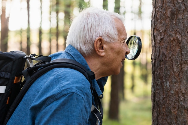 Free photo side view of older man in nature with magnifying glass