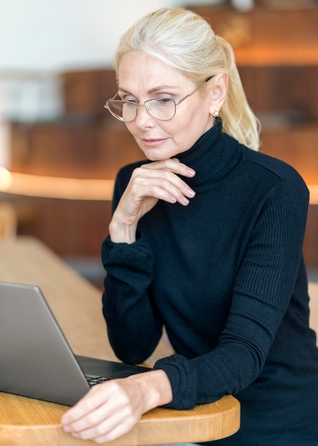 Side view of older woman wearing glasses and working on laptop