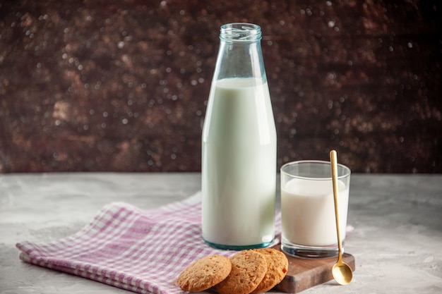 Side view of open glass bottle and cup filled with milk cookies on purple stripped towel on wooden cutting board