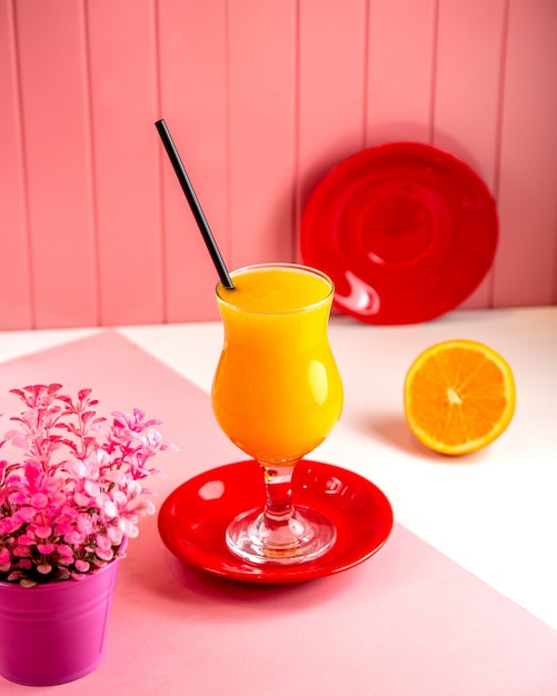 Free photo side view of orange fresh juice in glass on pink