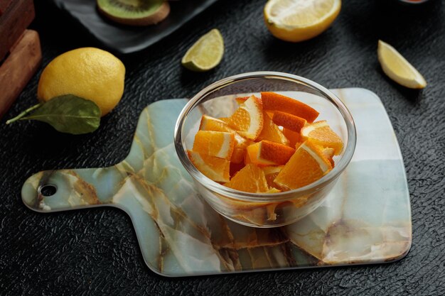 Side view of orange slices in bowl on cutting board with lemon on black background